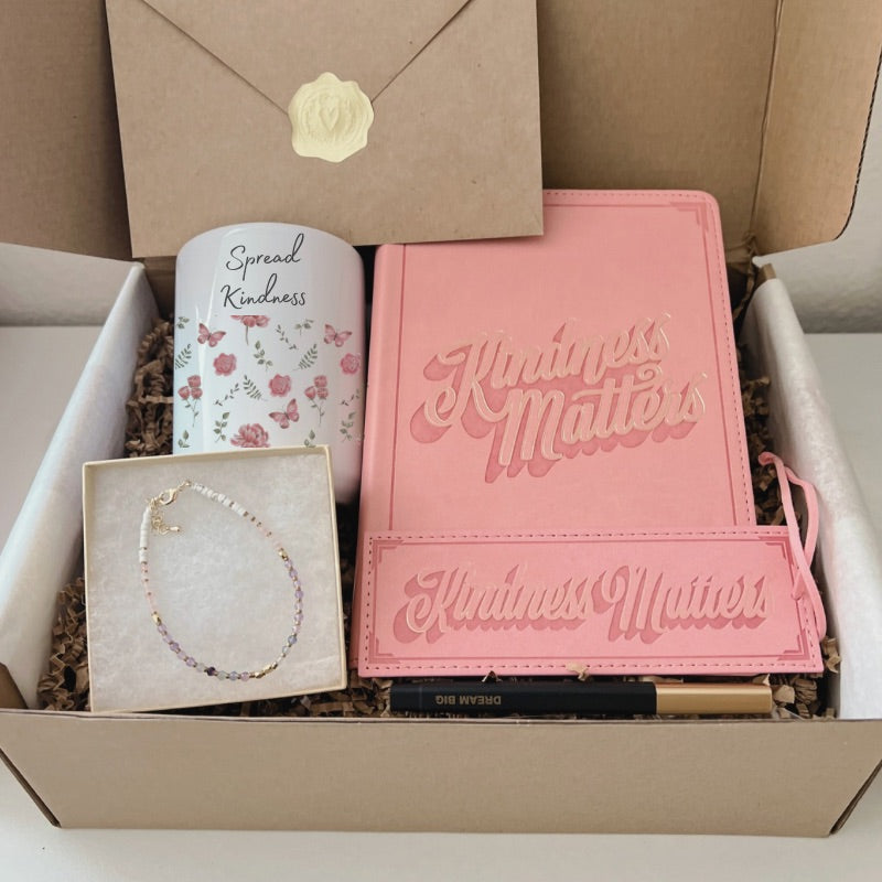 Kindness-themed gift box with floral mug, pink journal, bookmark, pen, intention bracelet, and affirmation card