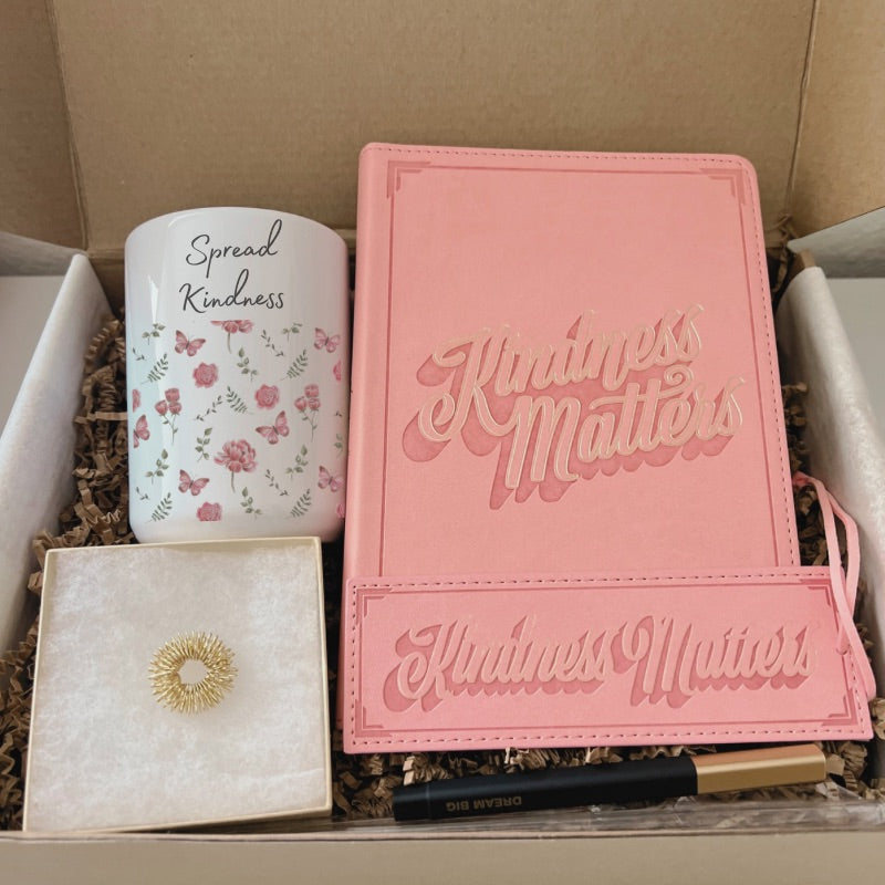Kindness-themed gift box with floral mug, pink journal, bookmark, pen, gold acupressure ring, and affirmation card